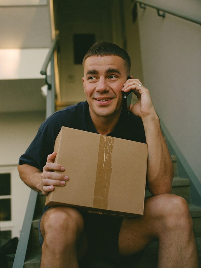 Resident sits on the stairs with a parcel on their lap and calls the parcel service