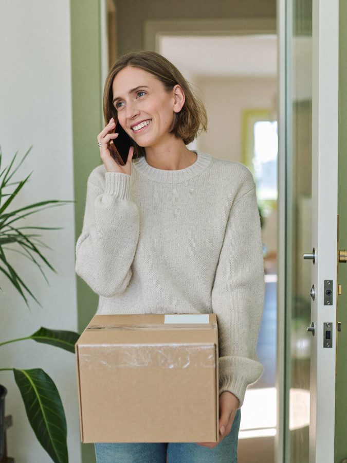 Customer takes a parcel at the front door, laughing, while calling the online shop